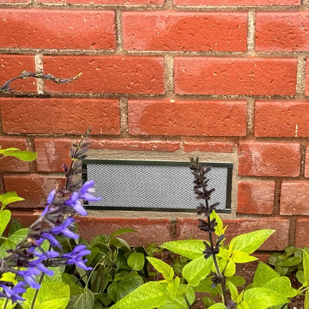 ember safe foundation vent installed in brick behind plants flowers